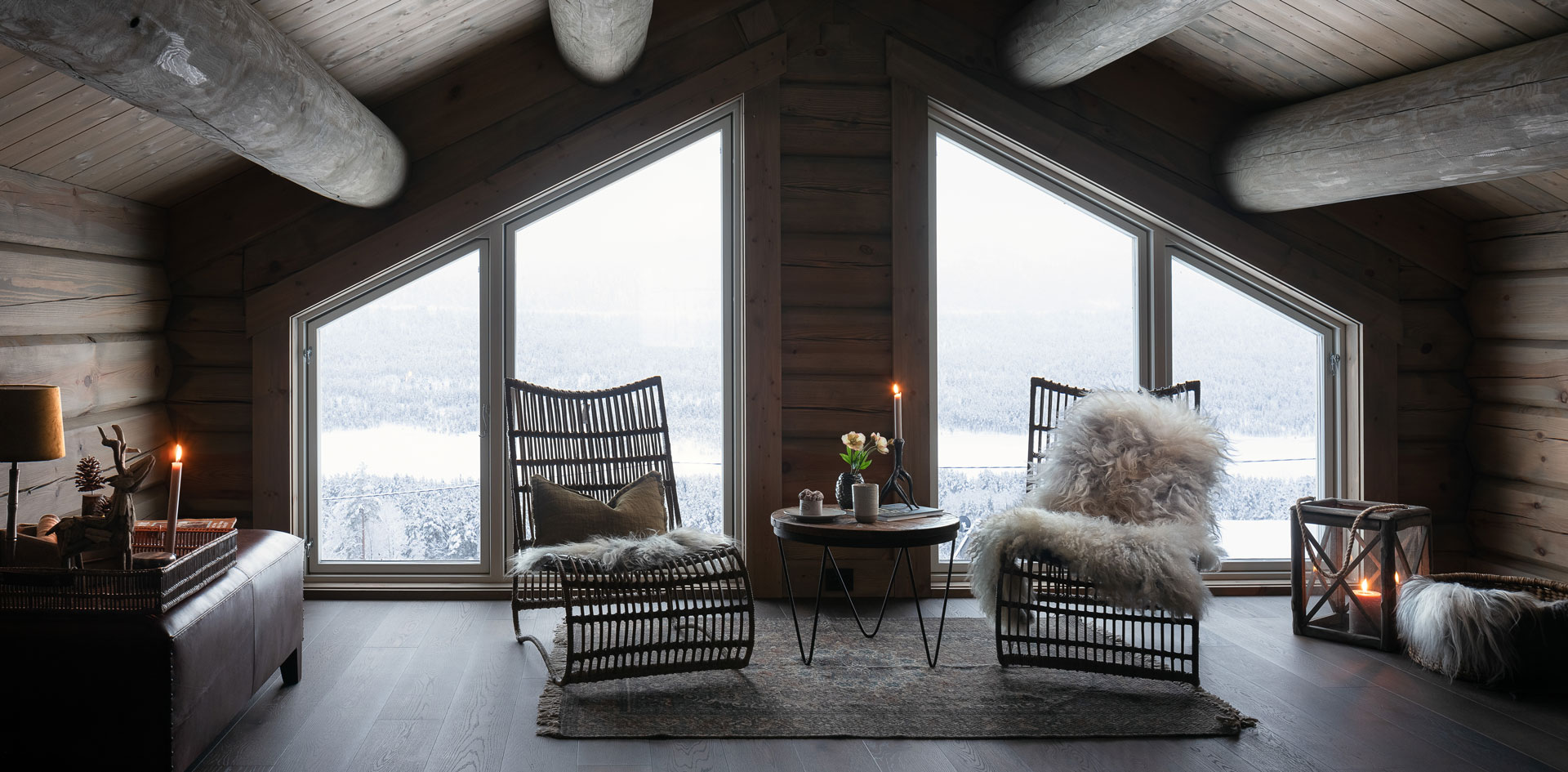 Interiør bilde av loftstue i fjellhytte, bygget av Geilo Laft AS. Koselig stemning med saueskinn, stearinlys og snødekket skog utenfor vinduet.